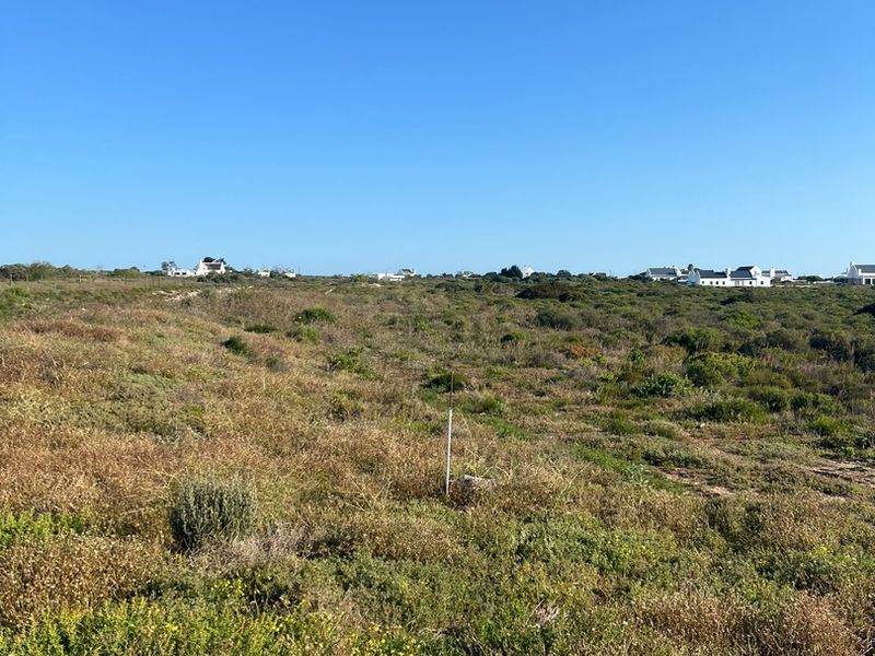 A view of a vacant residential plot featuring natural coastal vegetation and surrounding neighborhood homes in the distance.
