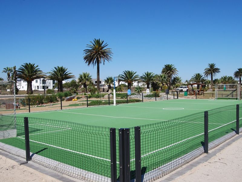 A well-maintained outdoor sports court featuring synthetic turf, perimeter fencing, and goal posts, set within a landscaped residential estate environment.