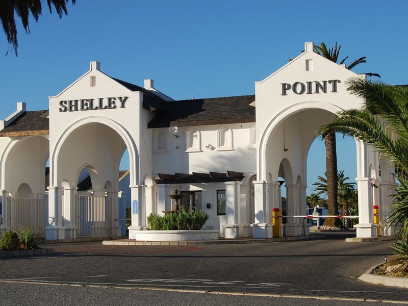 The main entrance gate to Shelley Point, featuring a grand white archway, security boom gates, and a paved driveway.