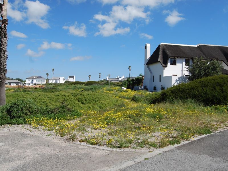 A view of a vacant residential plot featuring natural vegetation, with a neighboring thatched-roof property visible in the background.