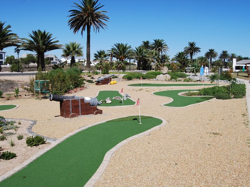 A well-maintained miniature golf course facility featuring synthetic turf greens, gravel pathways, and mature palm tree landscaping.