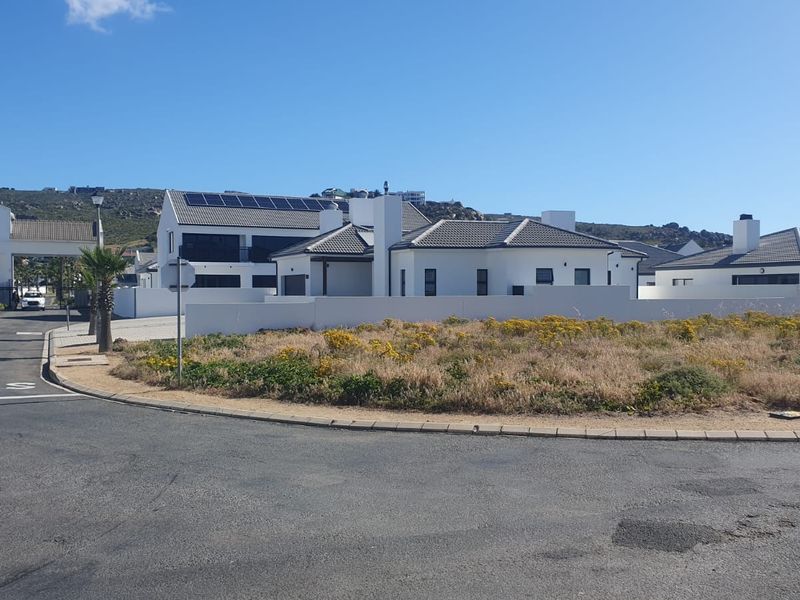 A street-level view of a modern residential property featuring a white facade, tiled roof, and installed solar panels within a secure estate.