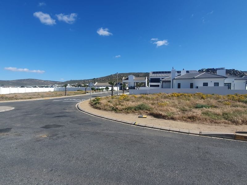 A view of the street and surrounding residential area, showcasing the paved road, curbing, and established boundary walls in a coastal estate setting.
