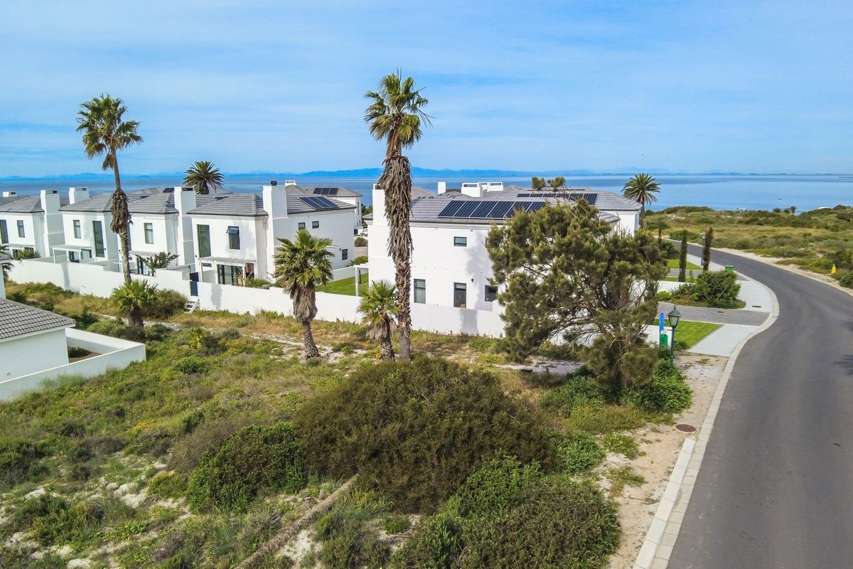 Aerial view of a residential estate featuring white modern homes with solar panels, situated near the coastline with surrounding natural vegetation.