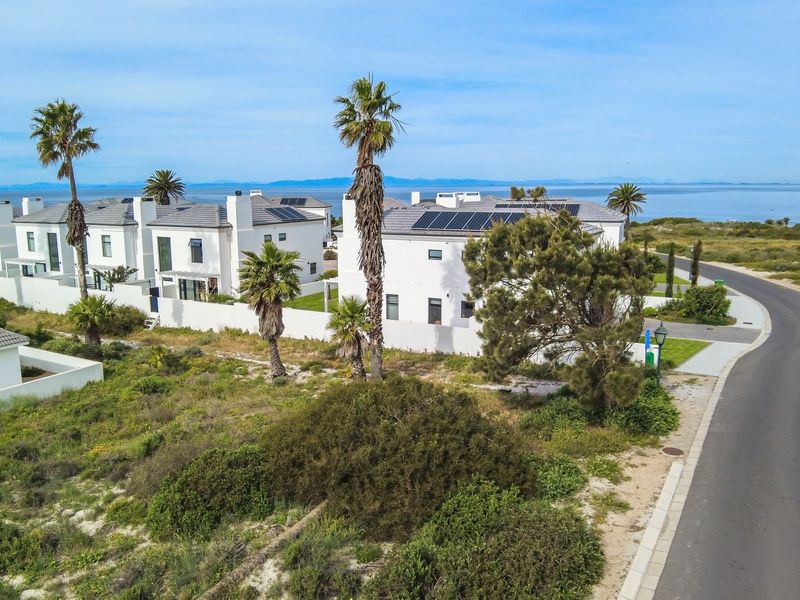 Aerial view of a residential estate featuring white modern homes with solar panels, situated near the coastline with surrounding natural vegetation.