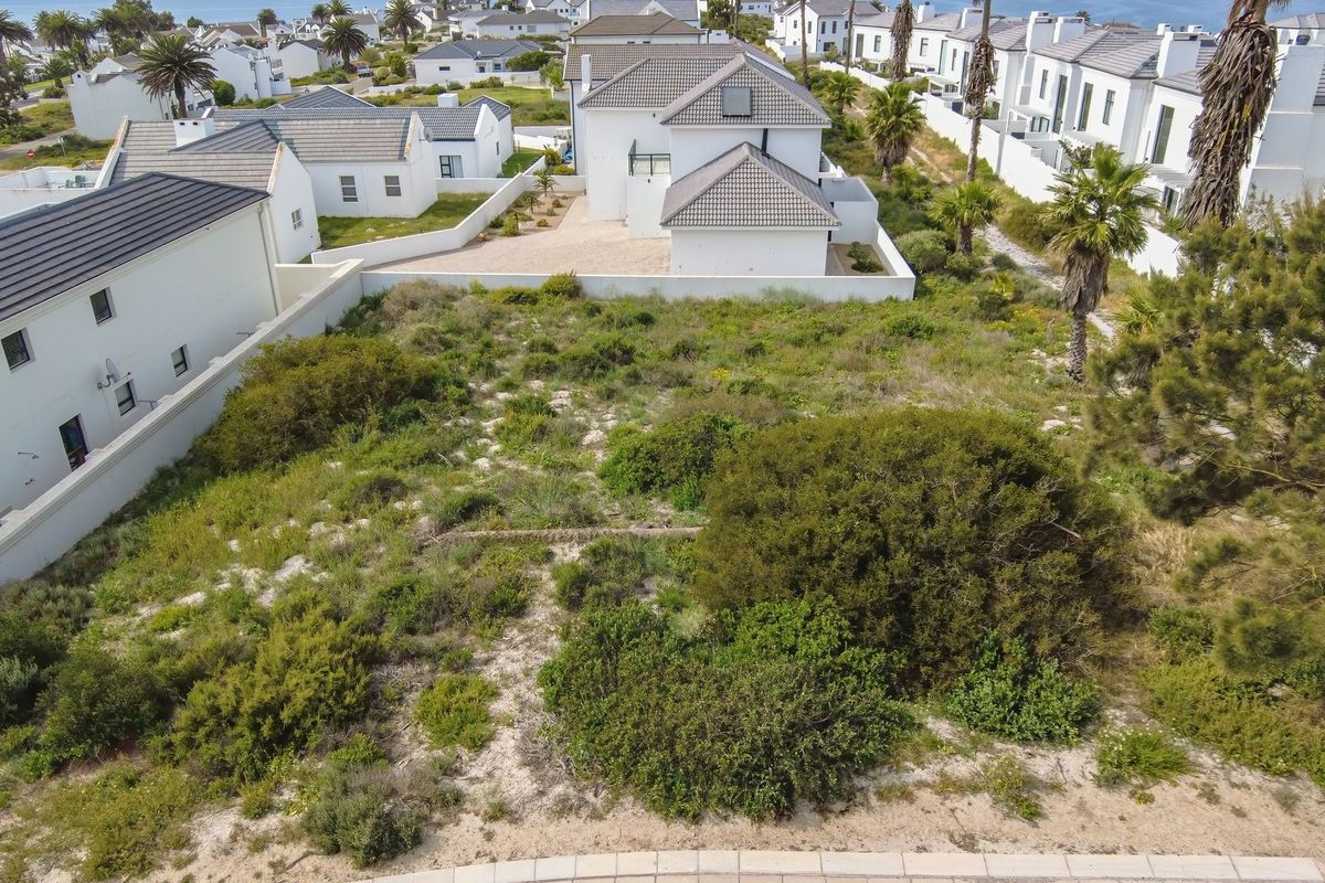 An aerial view of a vacant residential plot featuring native coastal vegetation and boundary walls, situated within a developed residential estate.