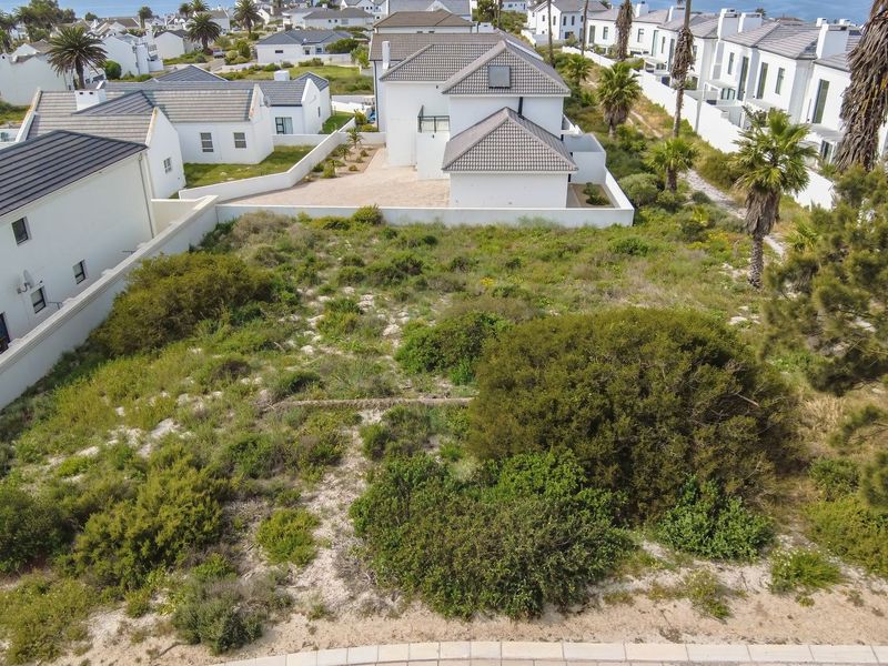 An aerial view of a vacant residential plot featuring native coastal vegetation and boundary walls, situated within a developed residential estate.