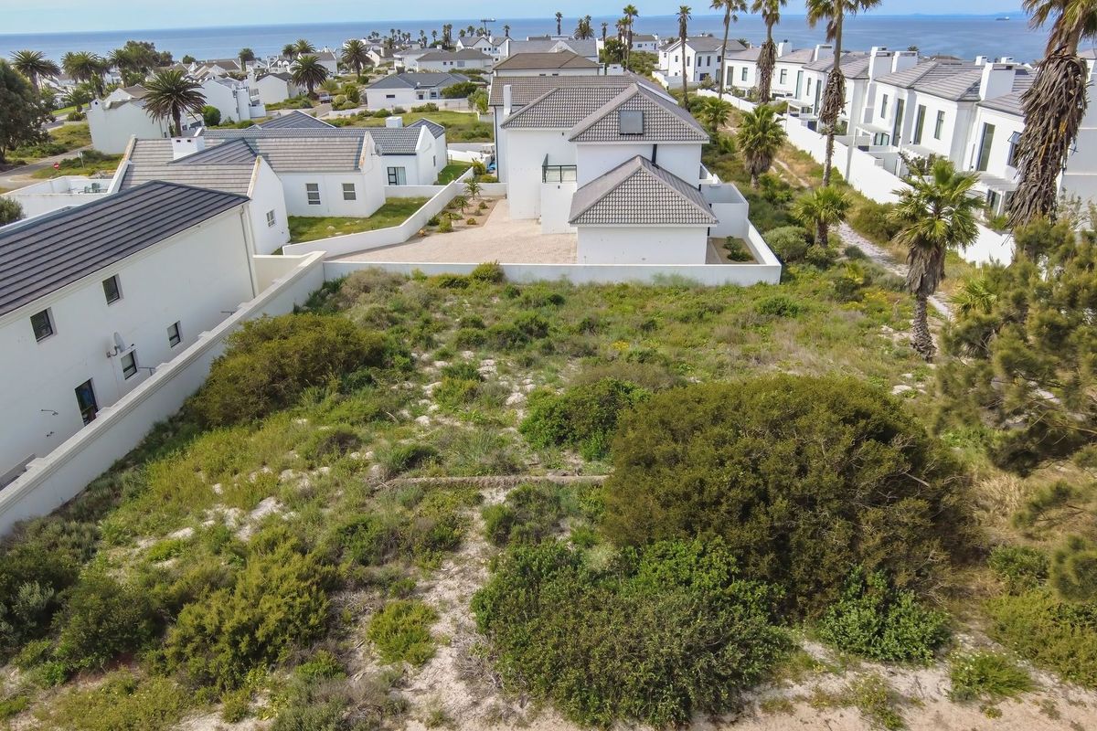An aerial view of a vacant residential plot situated within a coastal estate, surrounded by established homes and natural vegetation.
