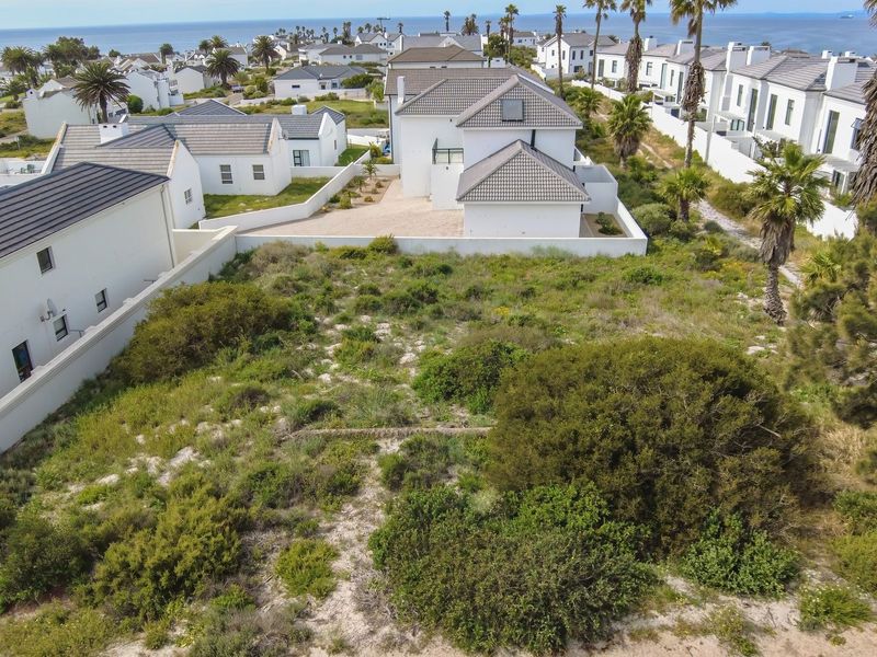 An aerial view of a vacant residential plot situated within a coastal estate, surrounded by established homes and natural vegetation.