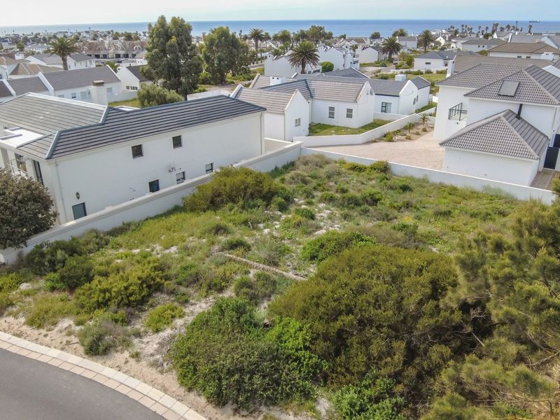 An aerial view of a vacant residential plot situated within a developed coastal estate, featuring surrounding homes and established vegetation.