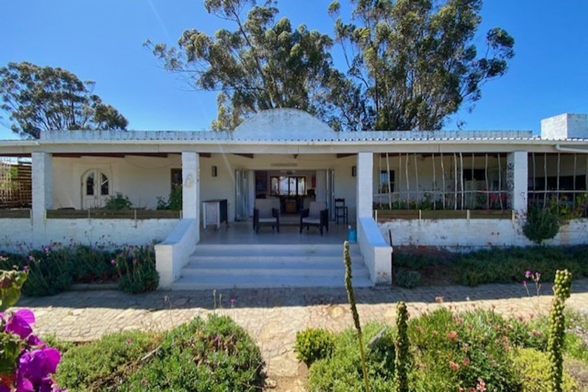 A rear view of the house featuring a covered patio with concrete steps, stone paving, and folding doors leading into the interior living space.