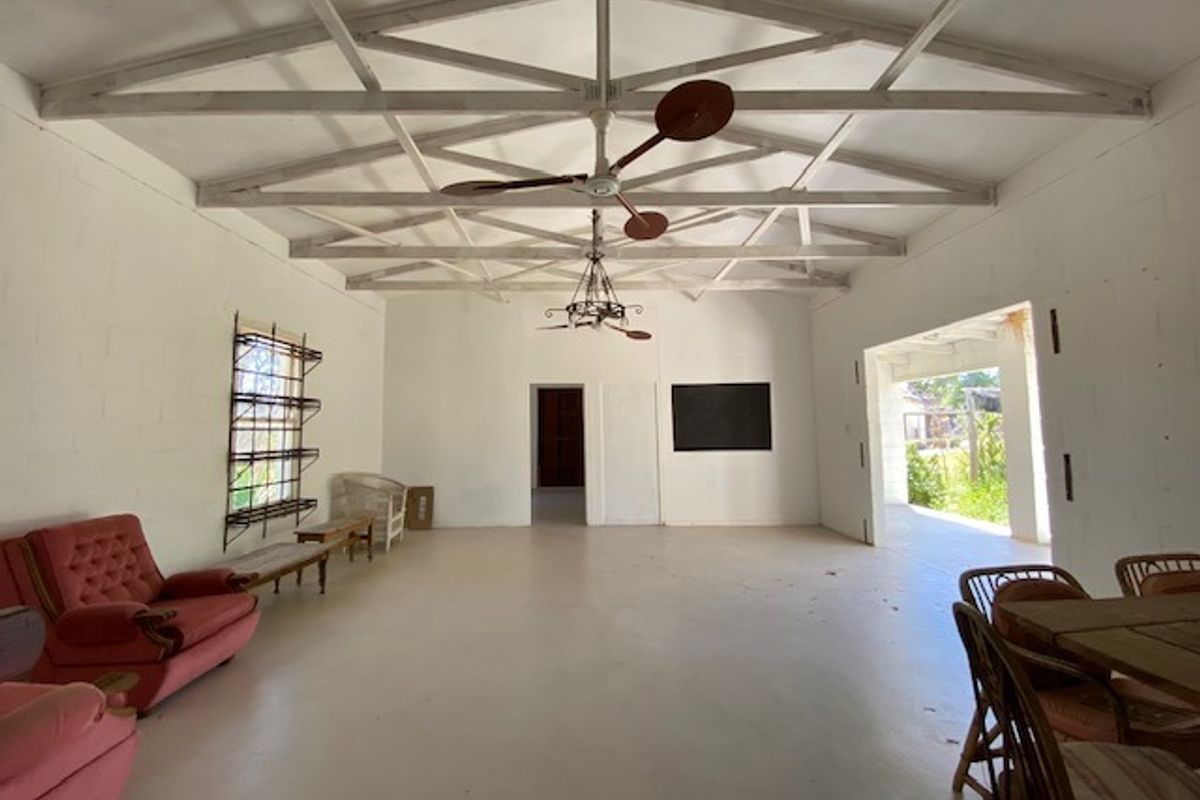 Spacious living area featuring exposed white-painted roof trusses, concrete block walls, and a large open-plan layout with direct access to an outdoor patio.