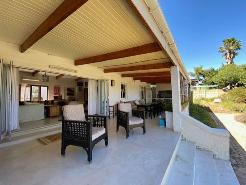 Spacious covered patio featuring exposed timber beams, built-in braai, and seamless access to the interior living area through large bi-fold doors.