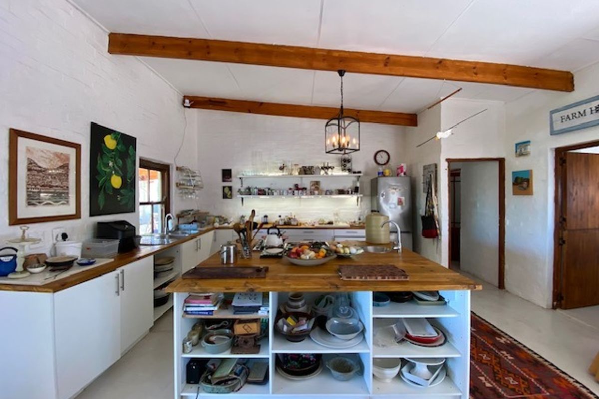 Spacious farmhouse-style kitchen featuring a large central timber island, exposed wooden ceiling beams, white cabinetry, and open shelving for storage.