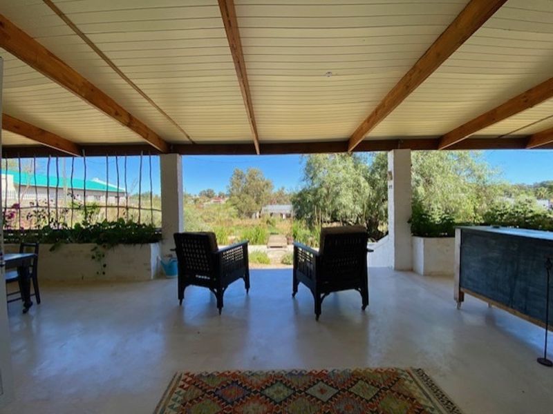 A spacious covered patio featuring a timber beam ceiling, concrete flooring, and built-in planter boxes, offering an open view of the surrounding landscape.