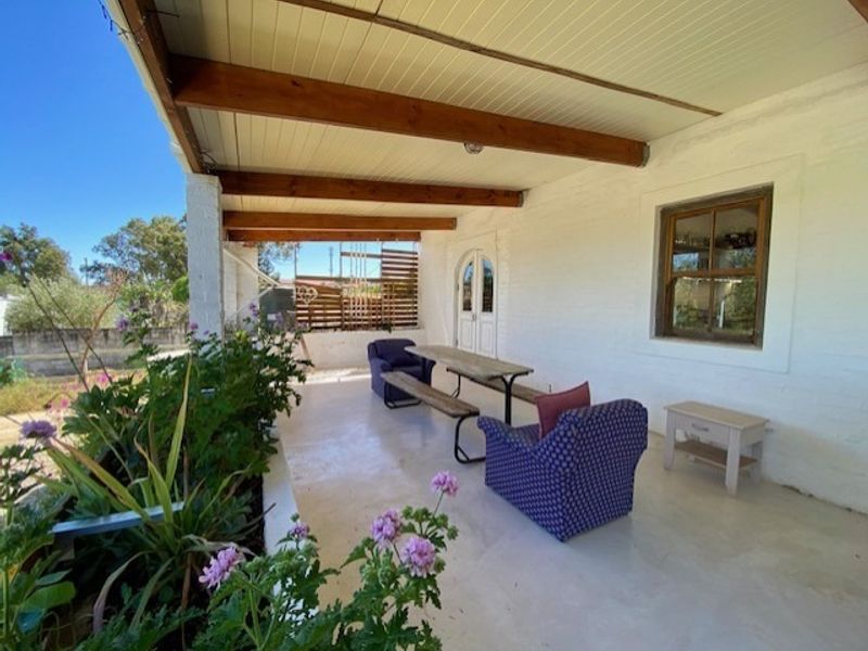 A covered outdoor patio featuring exposed timber beams, painted brick walls, and direct access to the garden through double doors.