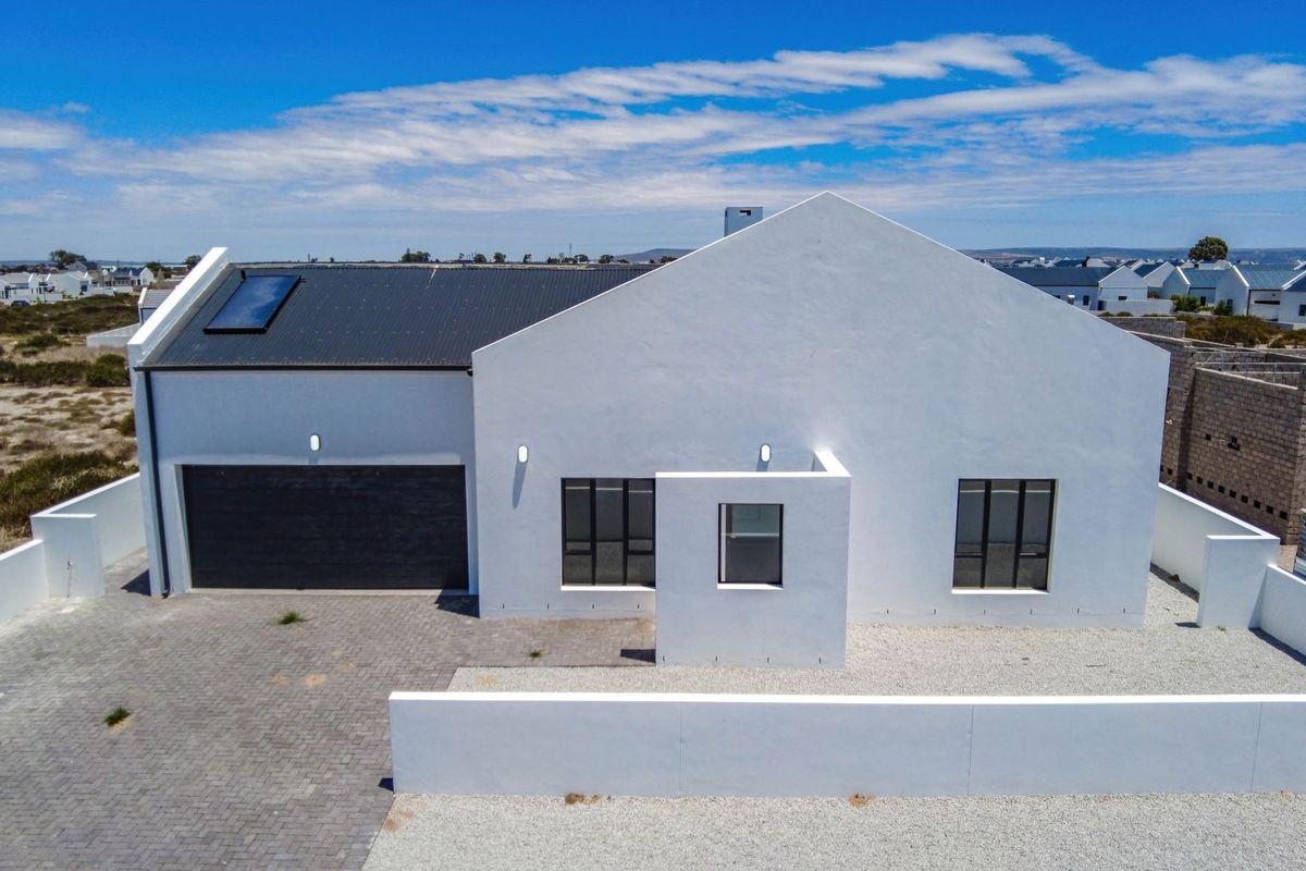 Aerial view of a modern white house featuring a corrugated metal roof, solar skylight, paved driveway, and secure boundary walling.