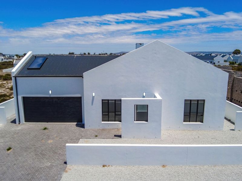 Aerial view of a modern white house featuring a corrugated metal roof, solar skylight, paved driveway, and secure boundary walling.