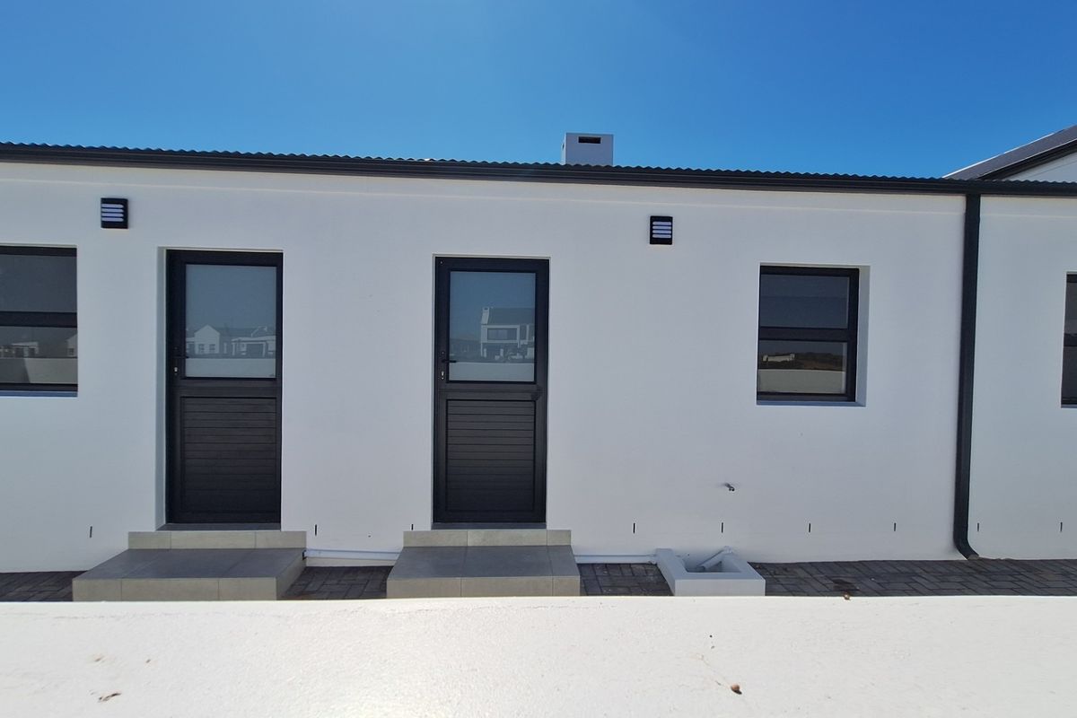 A clean rear exterior view of the property featuring modern white walls, dark aluminium window and door frames, and paved access steps.