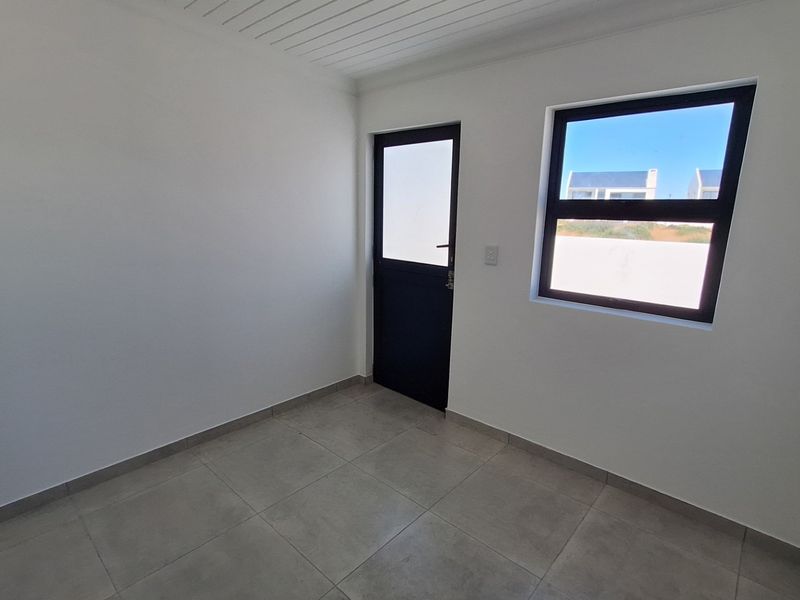 A clean, empty bedroom featuring neutral tiled flooring, white walls, and a modern dark-framed external door and window.