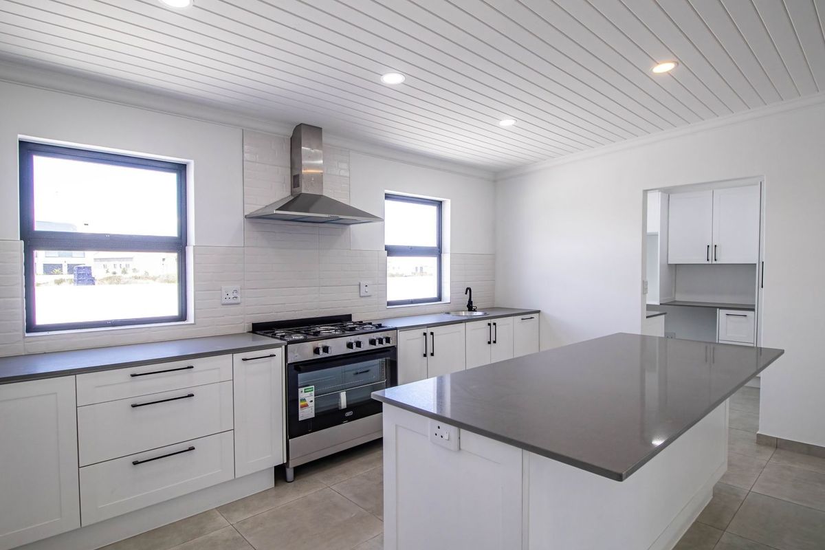 Modern kitchen featuring a central island, quartz countertops, stainless steel gas stove, extractor fan, and white shaker cabinetry with a tongue and groove ceiling.