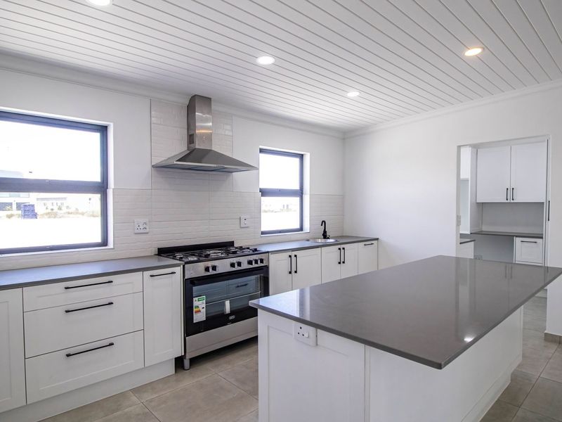 Modern kitchen featuring a central island, quartz countertops, stainless steel gas stove, extractor fan, and white shaker cabinetry with a tongue and groove ceiling.