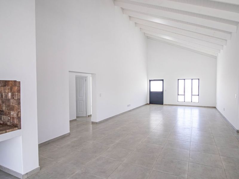 Spacious, light-filled living area featuring high vaulted ceilings with exposed rafters, tiled flooring, and a classic built-in brick fireplace.
