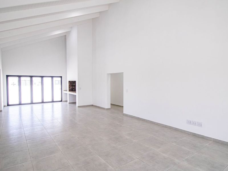 Spacious, light-filled living area featuring high vaulted ceilings with exposed beams, neutral tiled flooring, and large bi-fold doors leading to the exterior.