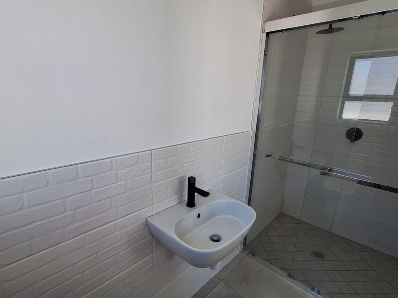 Modern bathroom featuring a wall-mounted basin with a black mixer tap and a spacious glass-enclosed shower with a rain shower head.