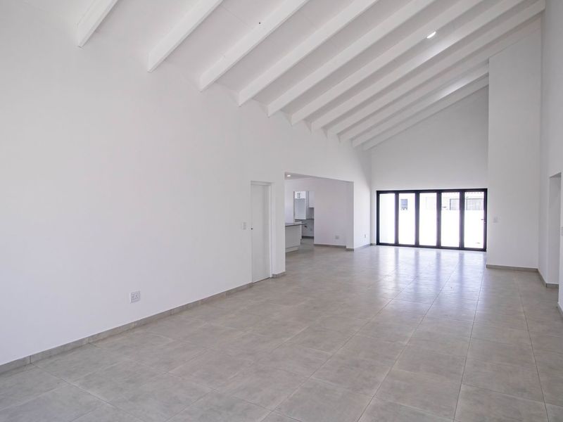 Spacious open-plan living area featuring high vaulted ceilings with exposed rafters, neutral tiled flooring, and large bi-fold doors leading to the exterior.
