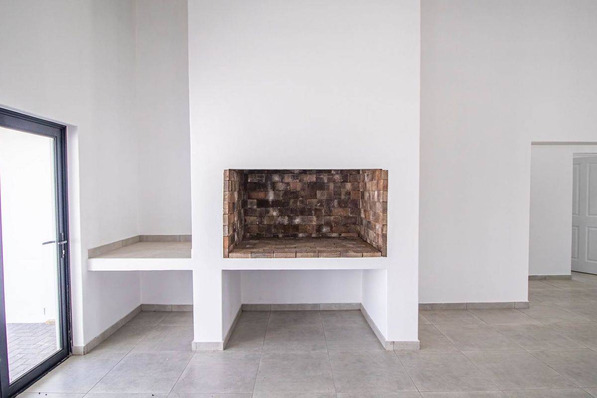 Spacious living area featuring a large built-in brick fireplace, neutral tiled flooring, and direct access to the exterior through a modern glass door.