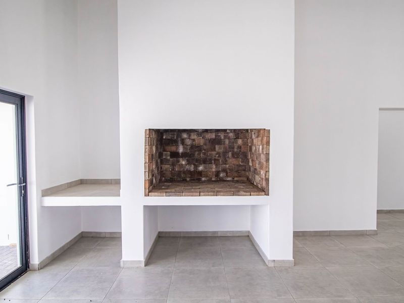 Spacious living area featuring a large built-in brick fireplace, neutral tiled flooring, and direct access to the exterior through a modern glass door.