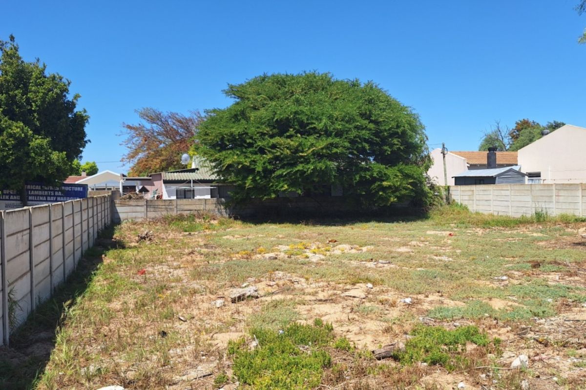 A vacant residential plot enclosed by precast concrete boundary walls, featuring natural ground cover and a mature tree.