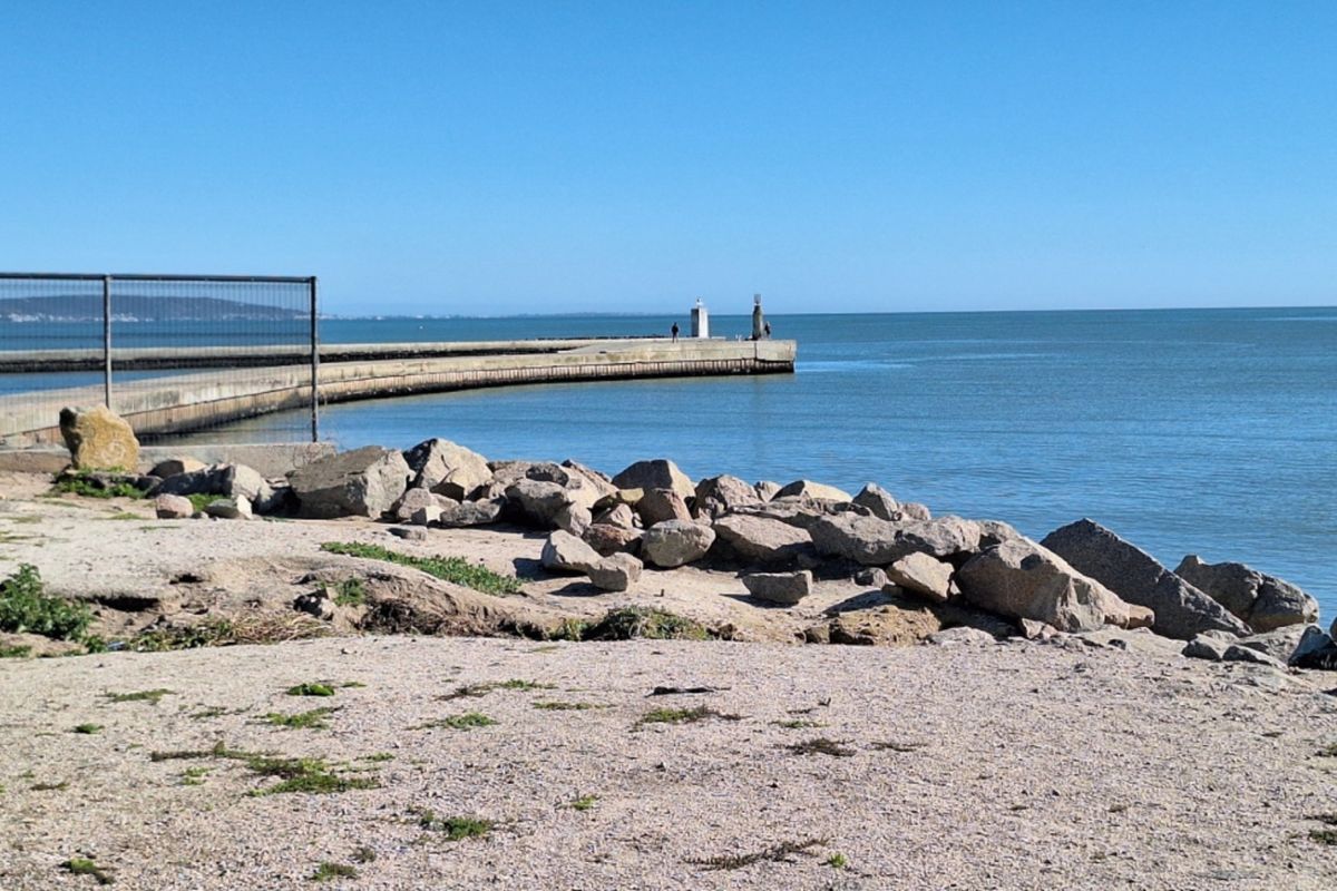 A scenic view of the coastline featuring a concrete pier extending into the ocean with natural rock formations along the shoreline.