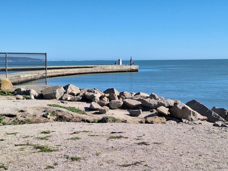A scenic view of the coastline featuring a concrete pier extending into the ocean with natural rock formations along the shoreline.