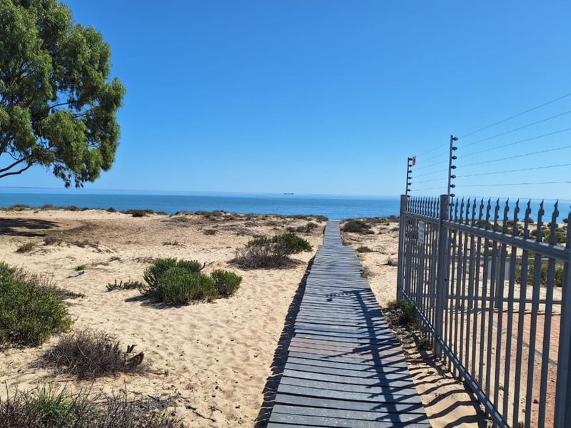 A scenic view of the coastline featuring a wooden boardwalk leading toward the ocean, secured by a metal fence with electric wiring.