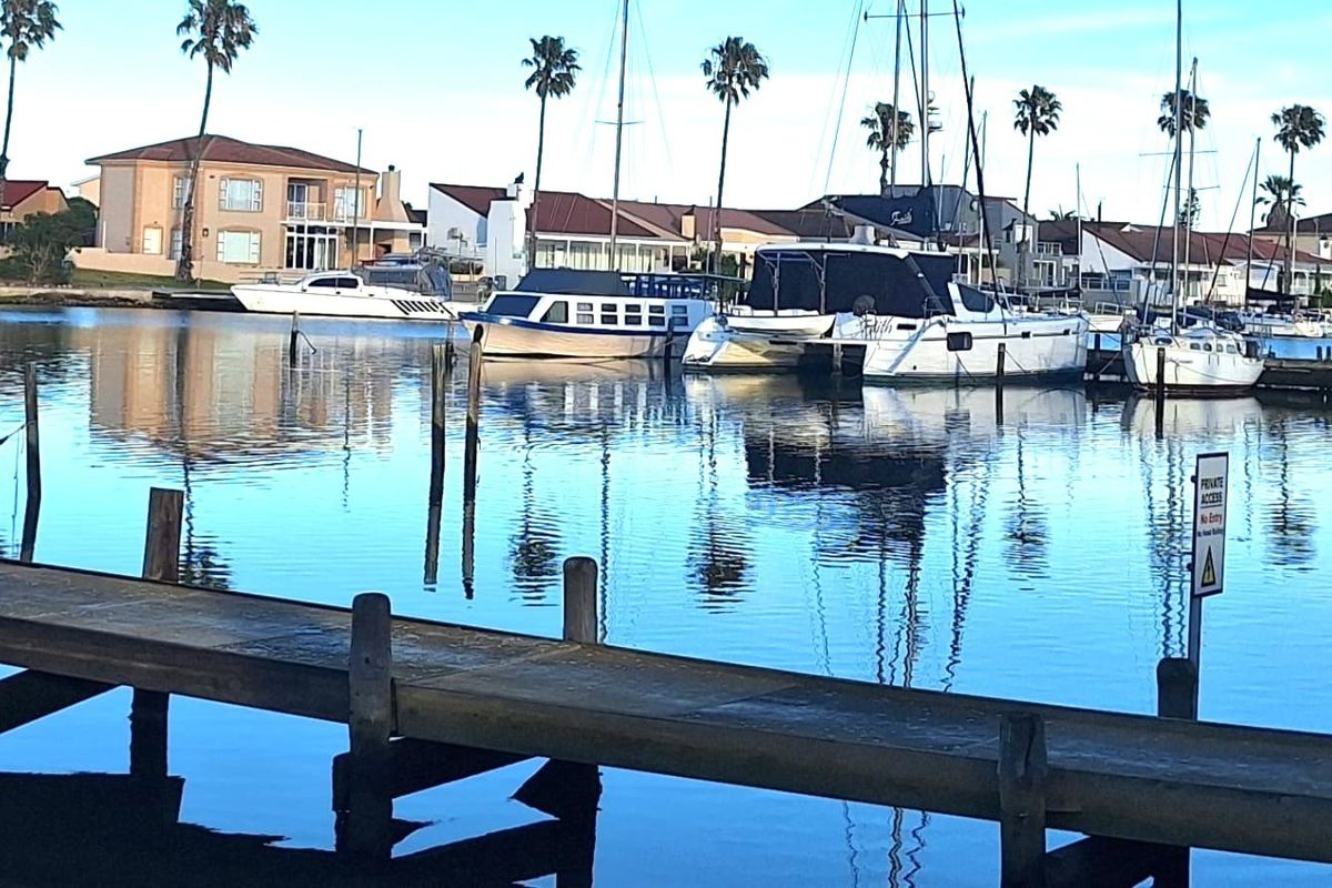 A scenic view of a calm marina with a wooden jetty in the foreground and residential properties in the background.