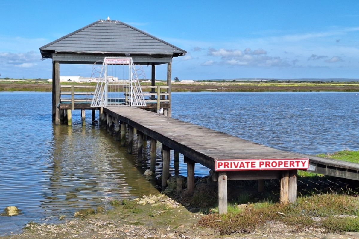 A wooden jetty extending into a calm body of water, featuring a covered gazebo structure and a secured entrance gate.
