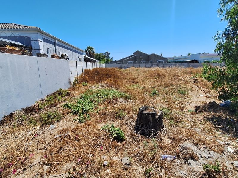 A vacant residential plot featuring a precast concrete boundary wall with security razor wire, requiring clearing and landscaping.