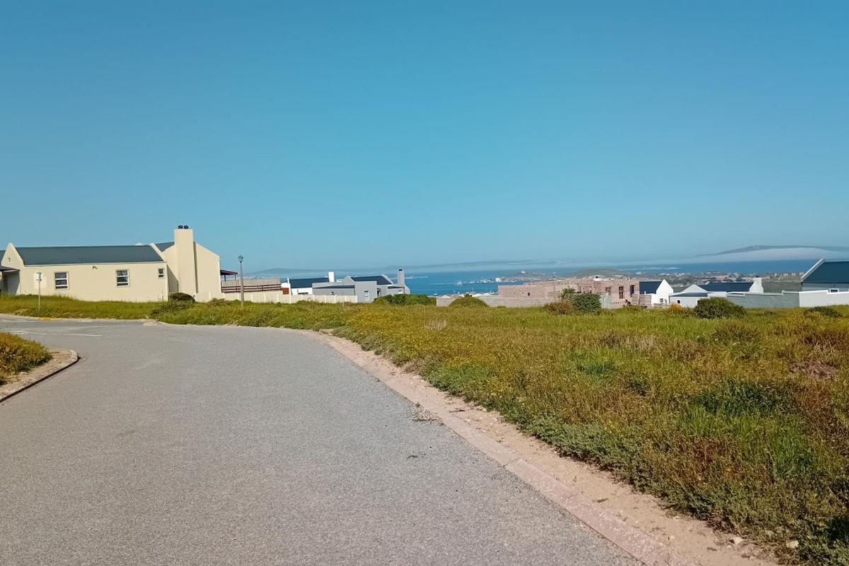 A street view of a residential vacant land plot featuring paved road access and distant coastal views.