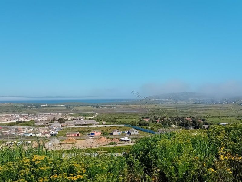 A wide-angle elevated view overlooking the surrounding landscape, residential area, and distant coastline under a clear blue sky.