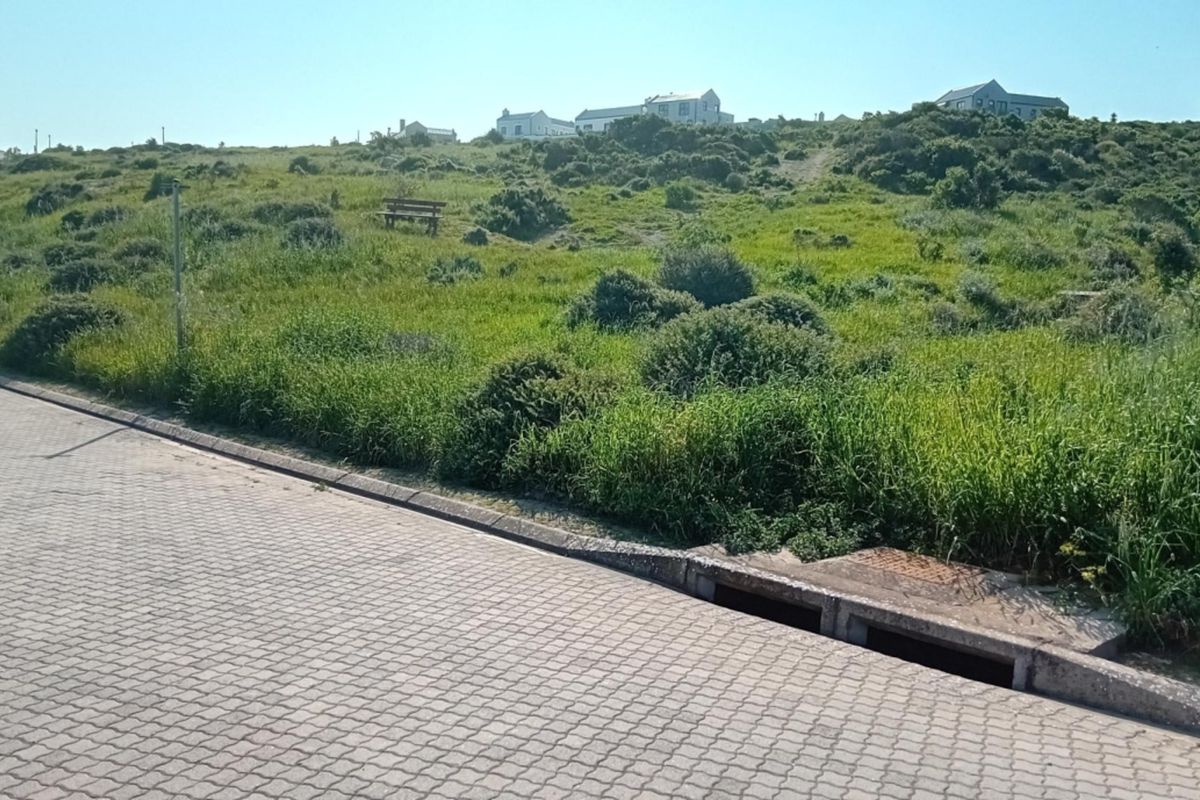 Street view of a vacant residential plot featuring paved road access, concrete kerbing, and integrated stormwater drainage infrastructure.