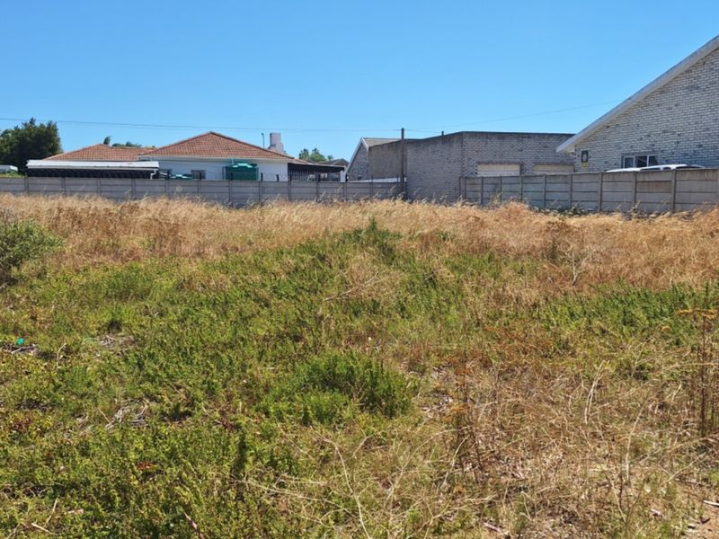 A vacant residential plot featuring dry grass and vegetation, enclosed by a precast concrete boundary wall in a suburban neighborhood setting.