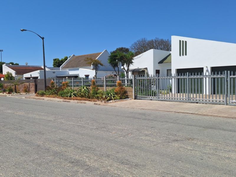 A street-level view of a residential property featuring modern white facades, secure metal fencing, and a paved driveway in a quiet neighborhood.
