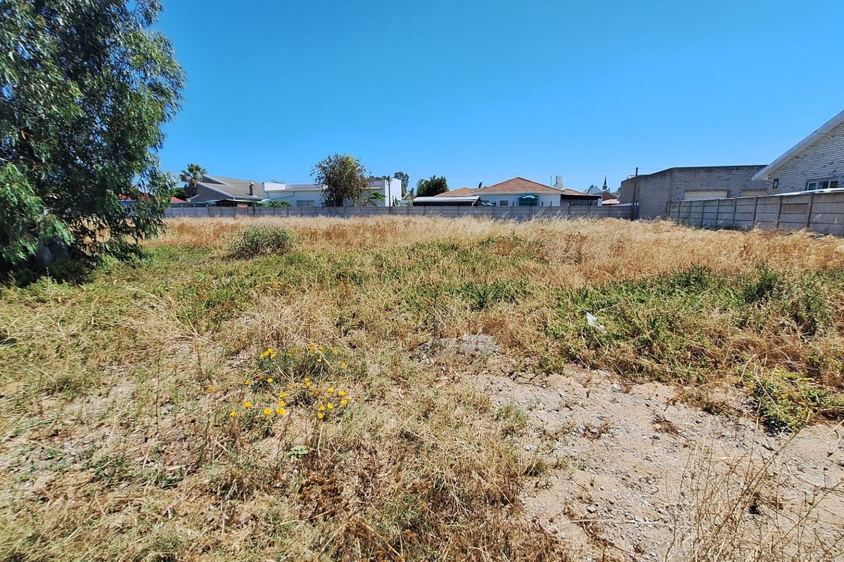 A vacant residential plot featuring dry, overgrown vegetation and enclosed by a precast concrete boundary wall.