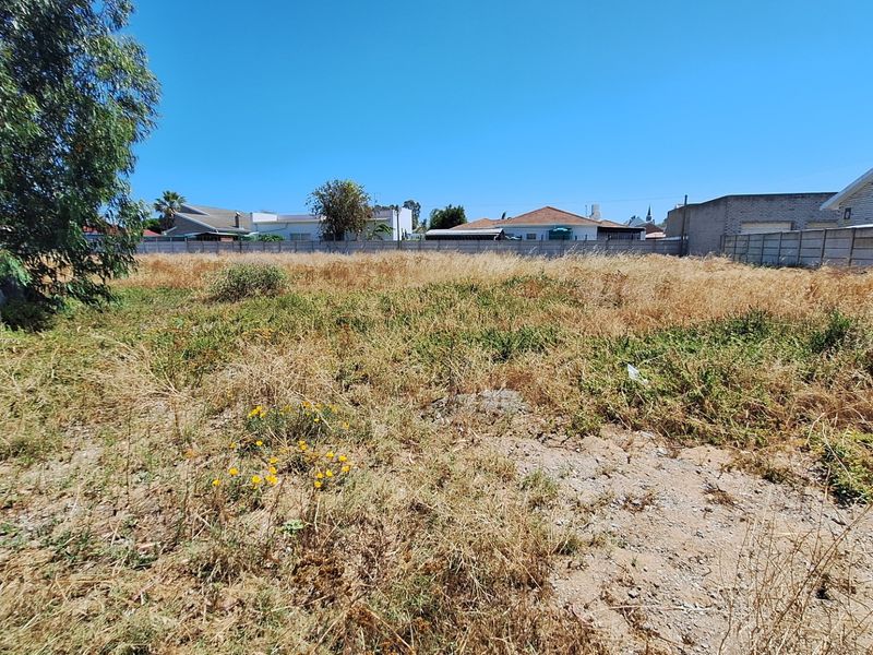 A vacant residential plot featuring dry, overgrown vegetation and enclosed by a precast concrete boundary wall.
