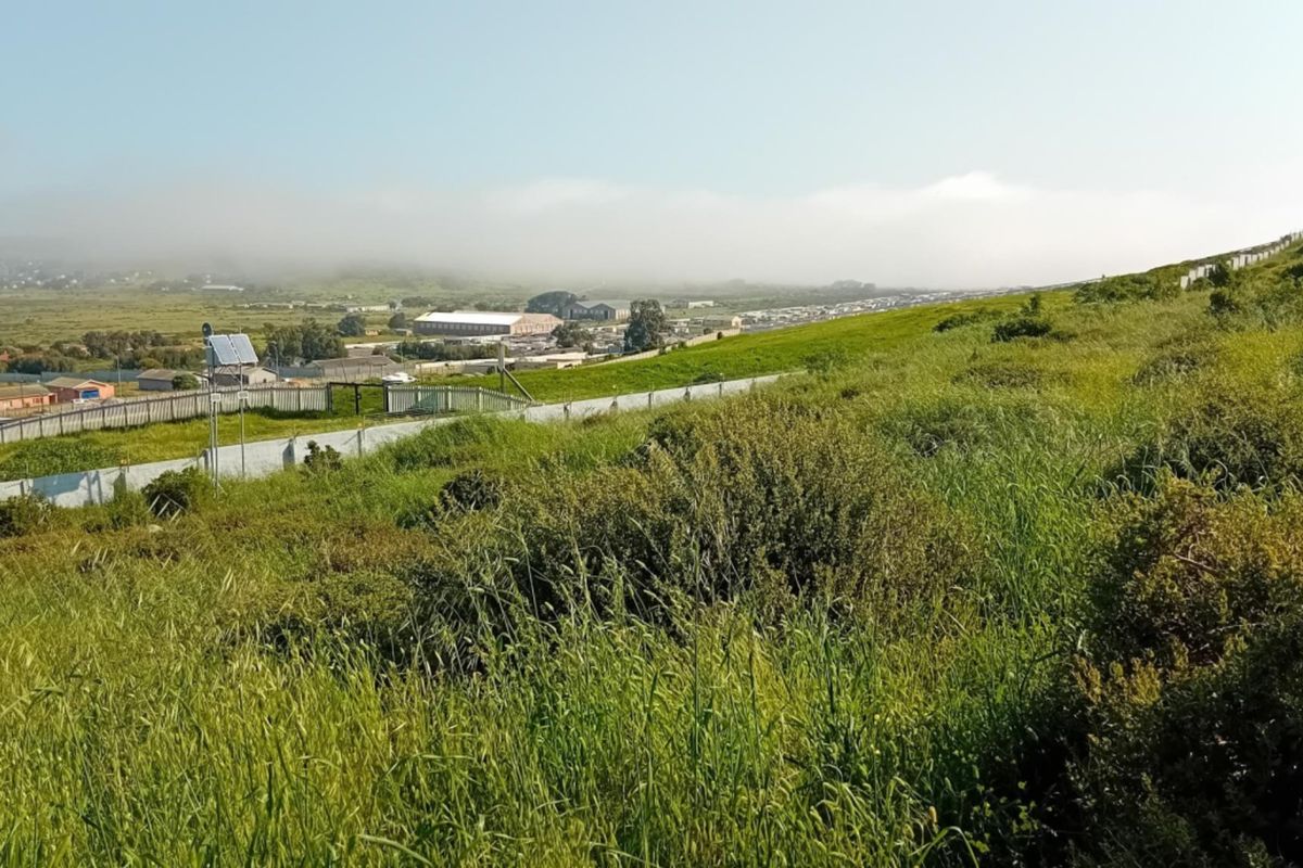 A view of the vacant residential land featuring natural sloped terrain and perimeter fencing, overlooking the surrounding neighborhood and landscape.