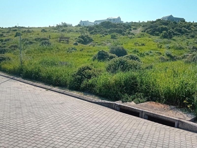 Street view of a vacant residential plot featuring paved road access, concrete kerbing, and integrated stormwater drainage infrastructure.