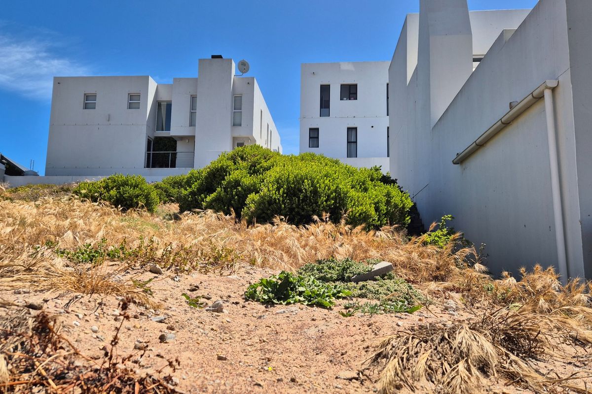 A view of the rear section of the vacant residential plot, showing the adjacent multi-story residential buildings and boundary walling.