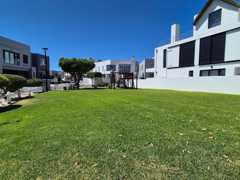 A well-maintained residential lawn area featuring a boundary wall and playground equipment within a modern estate setting.